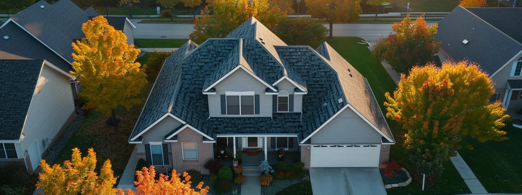Aerial view of a two-story house with a blue roof, surrounded by autumn trees and a driveway.