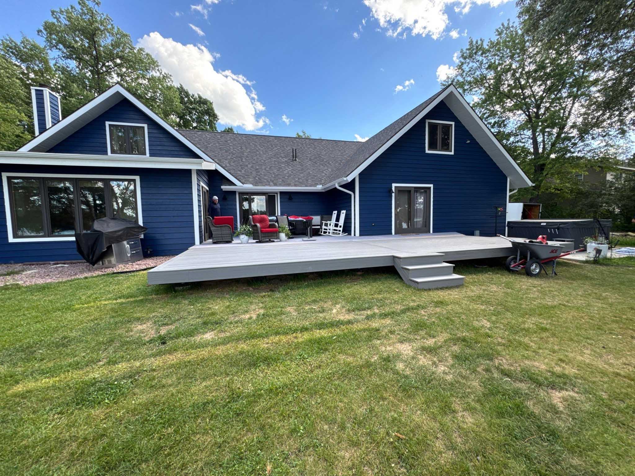 Blue house with gray composite deck by a top Wisconsin builder, grill, chairs, lawn and trees.