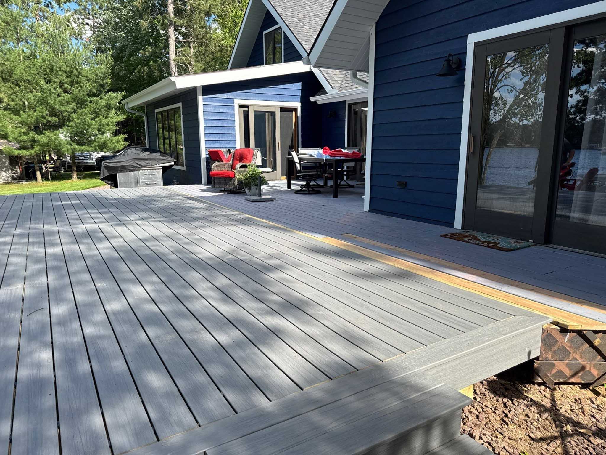 Gray deck by Composite Deck Builder Wisconsin with grill, furniture, and nearby blue house.