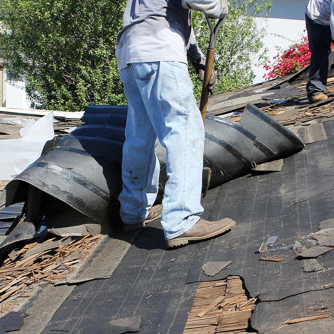 Person removing old roof shingles with a tool, debris scattered around a Wisconsin home’s siding.