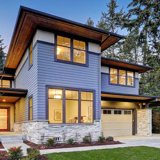 Modern Wisconsin two-story house with blue siding, large windows, and a beige garage door at dusk.