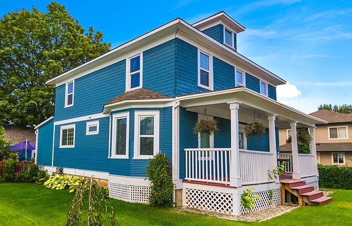 Blue two-story house with white trim, porch, new gutters, lush lawn, trees, and clear sky.