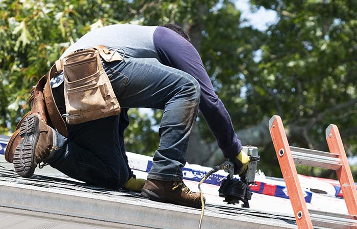 Person kneeling on roof, using a tool, with Horizon Exteriors siding and Wisconsin trees behind.