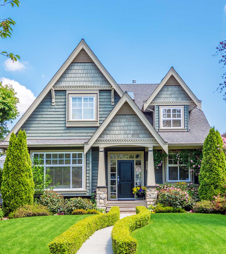 Two-story green house by Horizon Exteriors with new gutters, bushes, flowers, and a curved walkway.