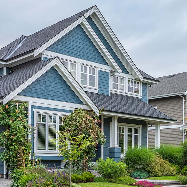 Blue two-story house with white trim by Horizon Exteriors, featuring new roofing and front garden.