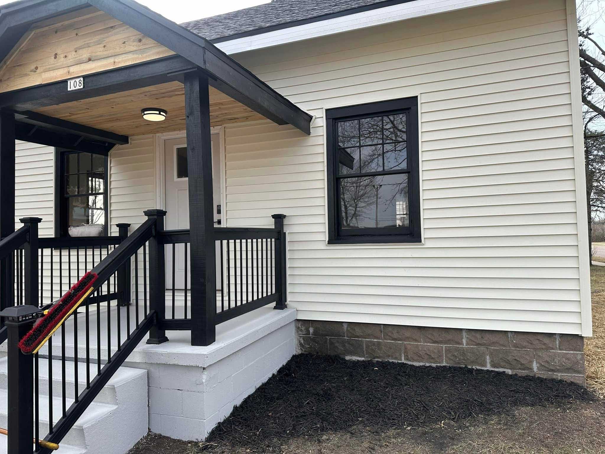 Small white house with black trim, porch railing, and quality siding by a top Wisconsin contractor.