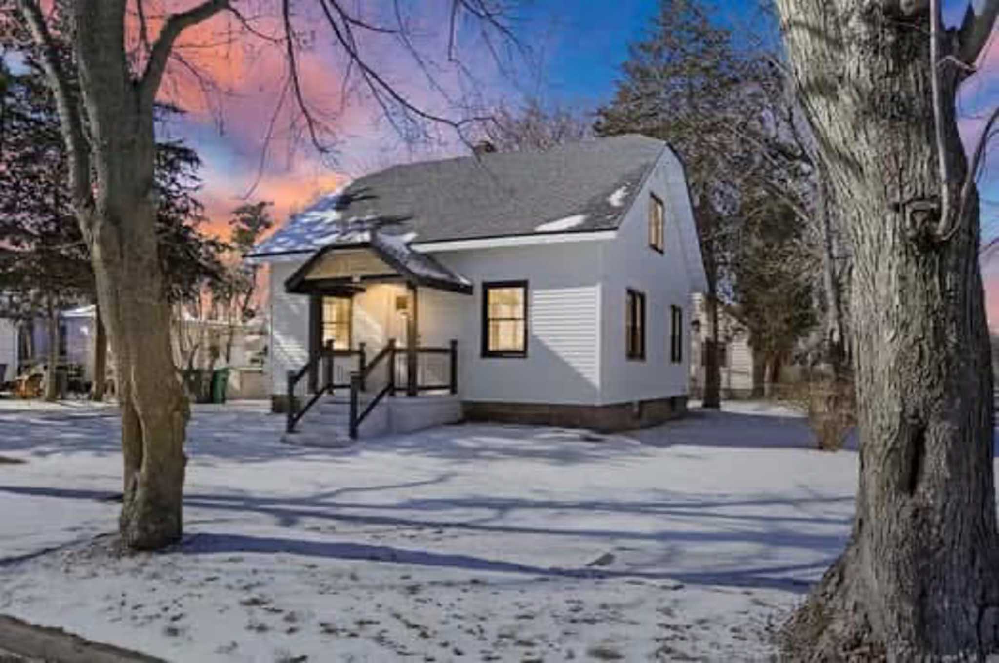 White house with black trim, snowy yard, trees—Siding Contractor Wisconsin for stunning results.