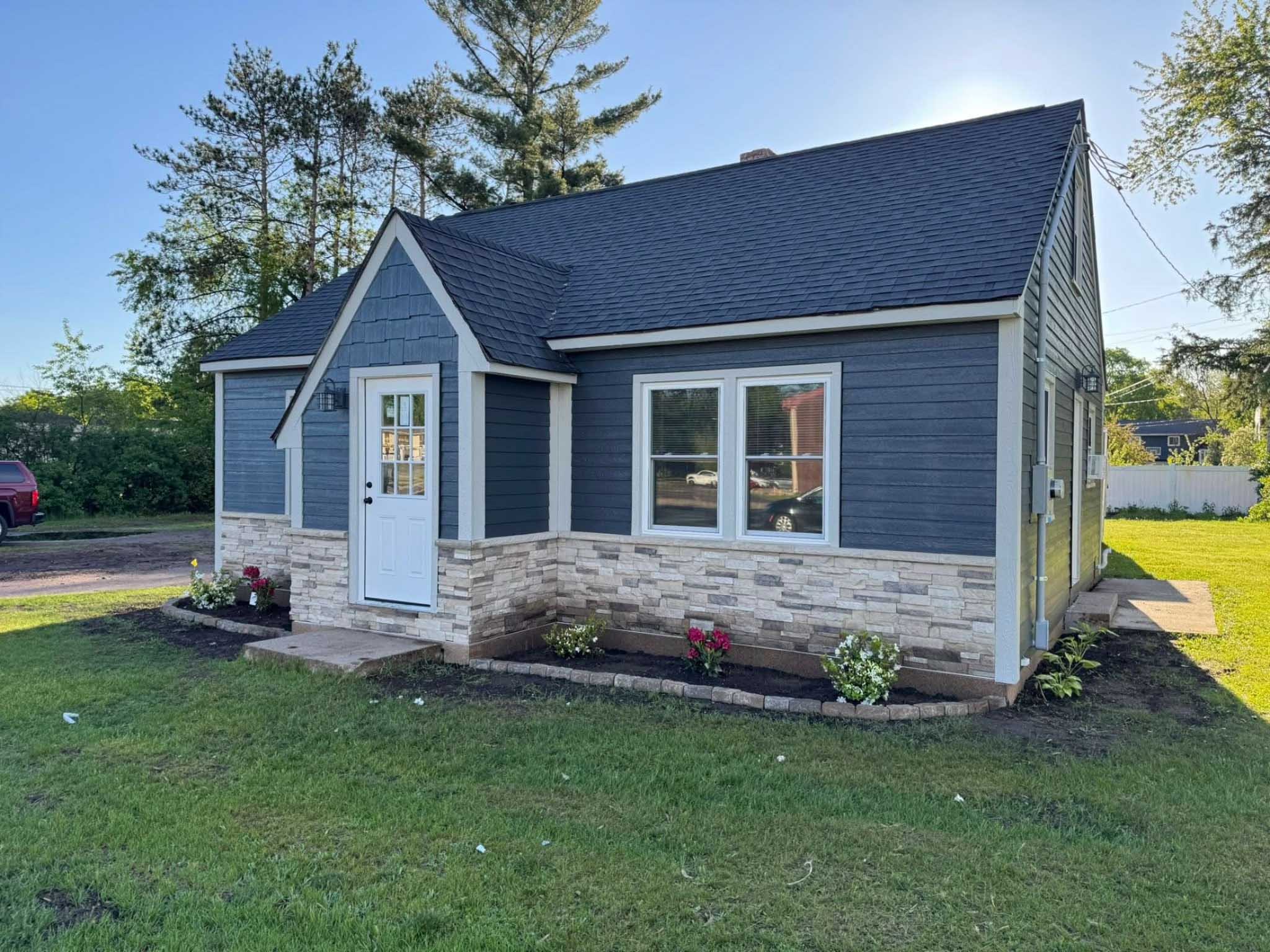 Blue house with white trim by top WI siding contractor; stone accents, flowers shine.
