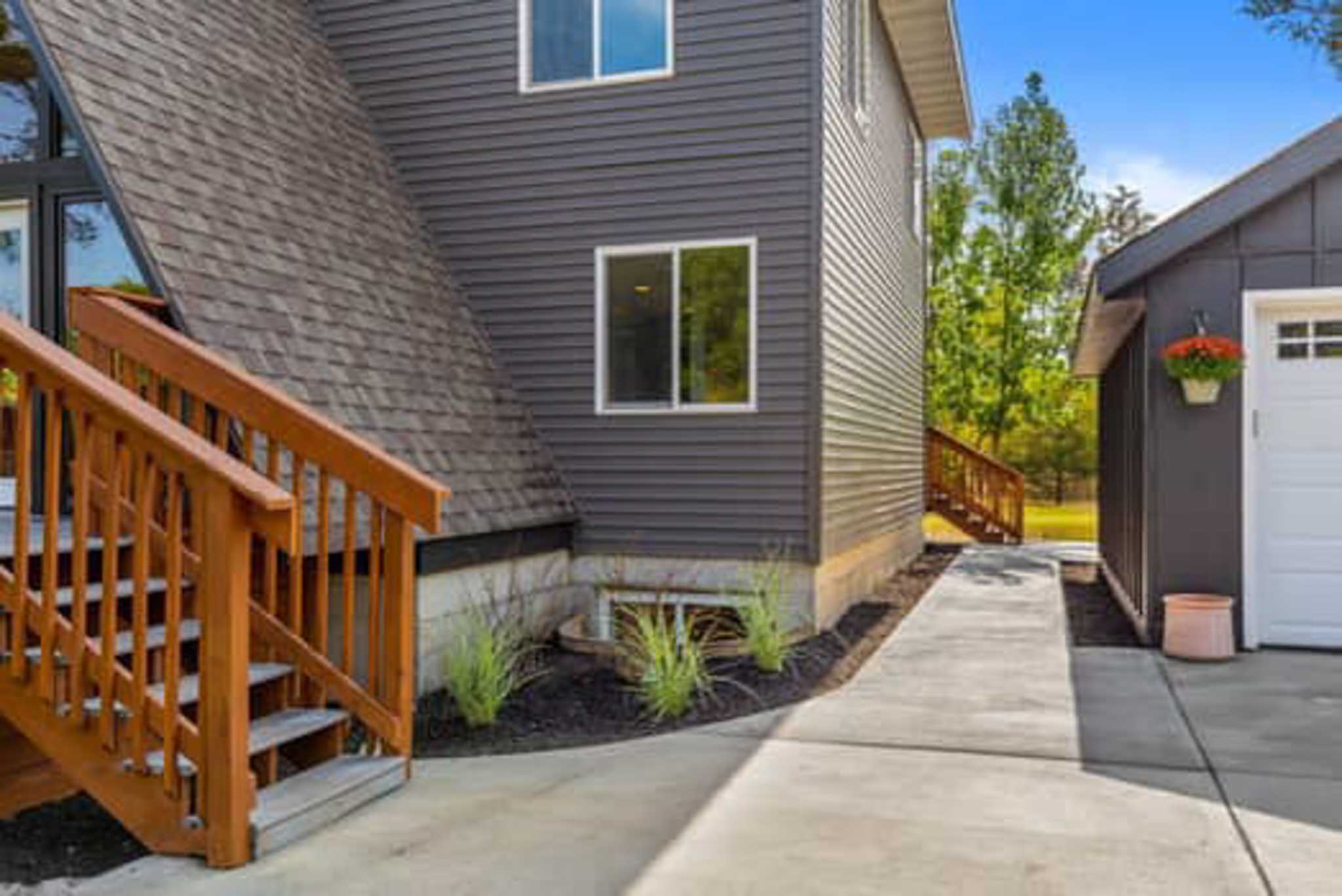 Gray house with wooden stairs, concrete path, garage, potted plant; siding contractor Wisconsin.