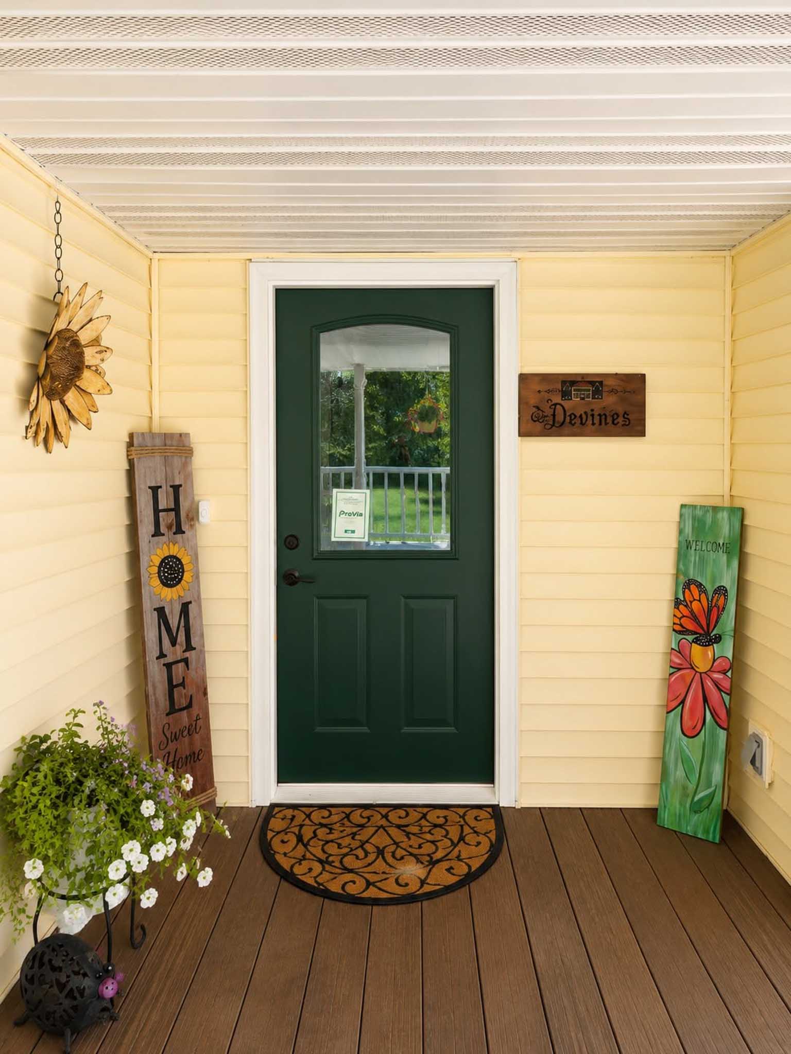 Green door, yellow siding, flower decor, HOME sign, and Replacement Windows Wisconsin porch.