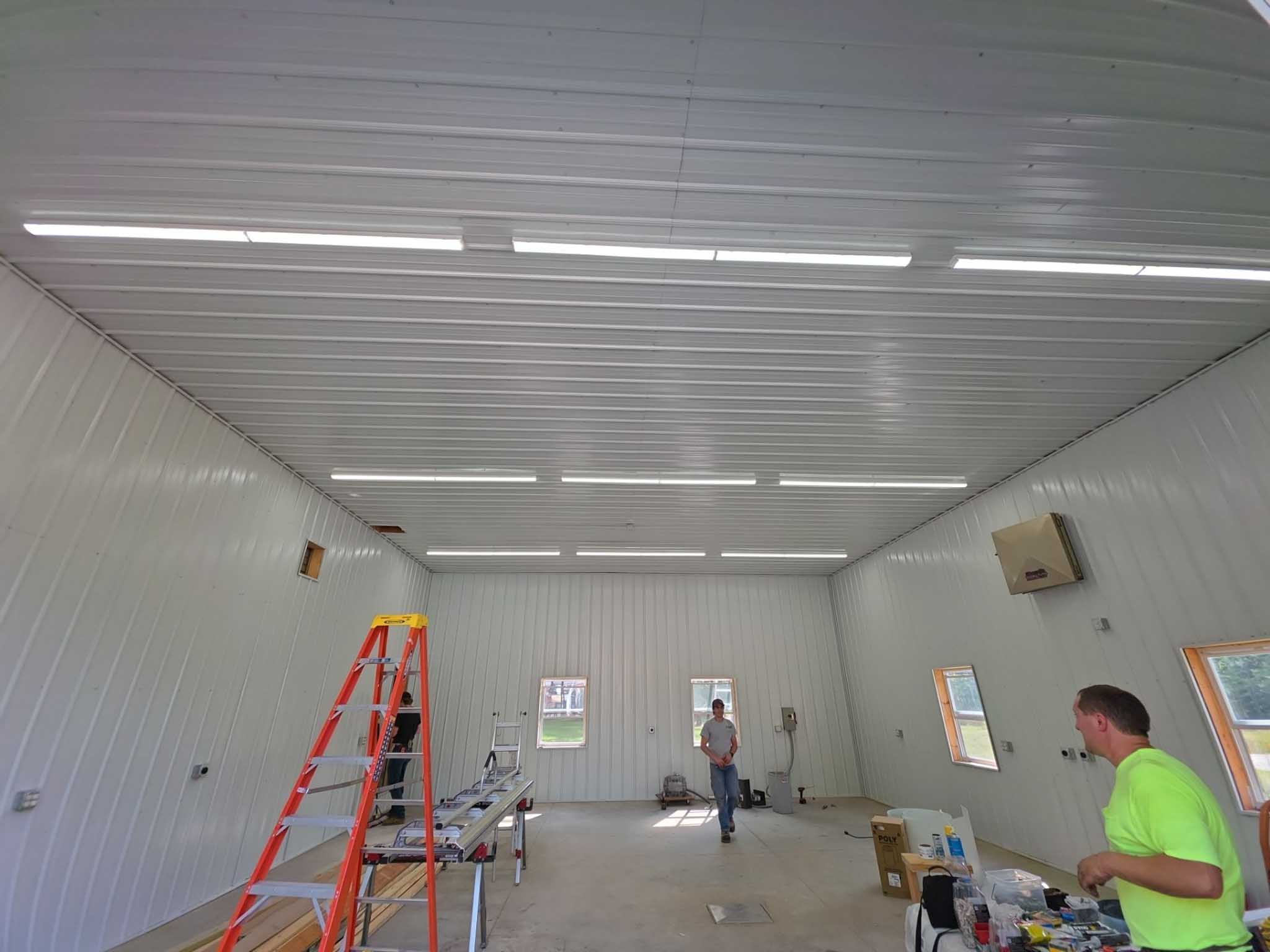 Two people work in a large, white room with tools, a ladder, and Replacement Windows Wisconsin.
