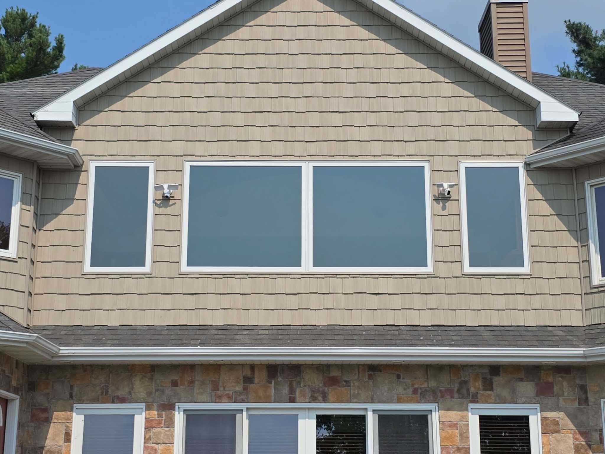 Second-story windows with closed blinds on a beige house; Replacement Windows Wisconsin nearby.