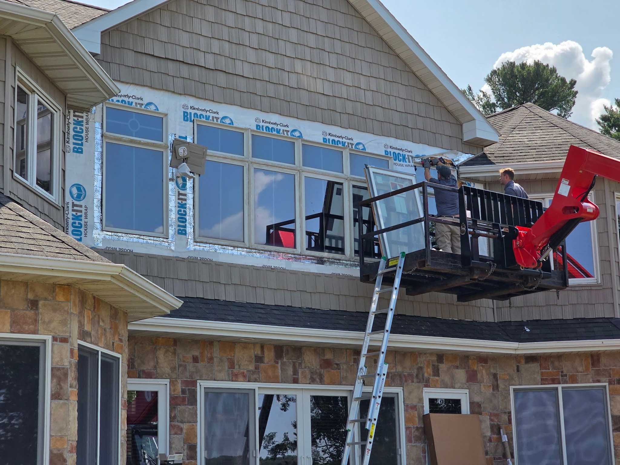 Workers install Replacement Windows Wisconsin on a second story using a lift and ladder.