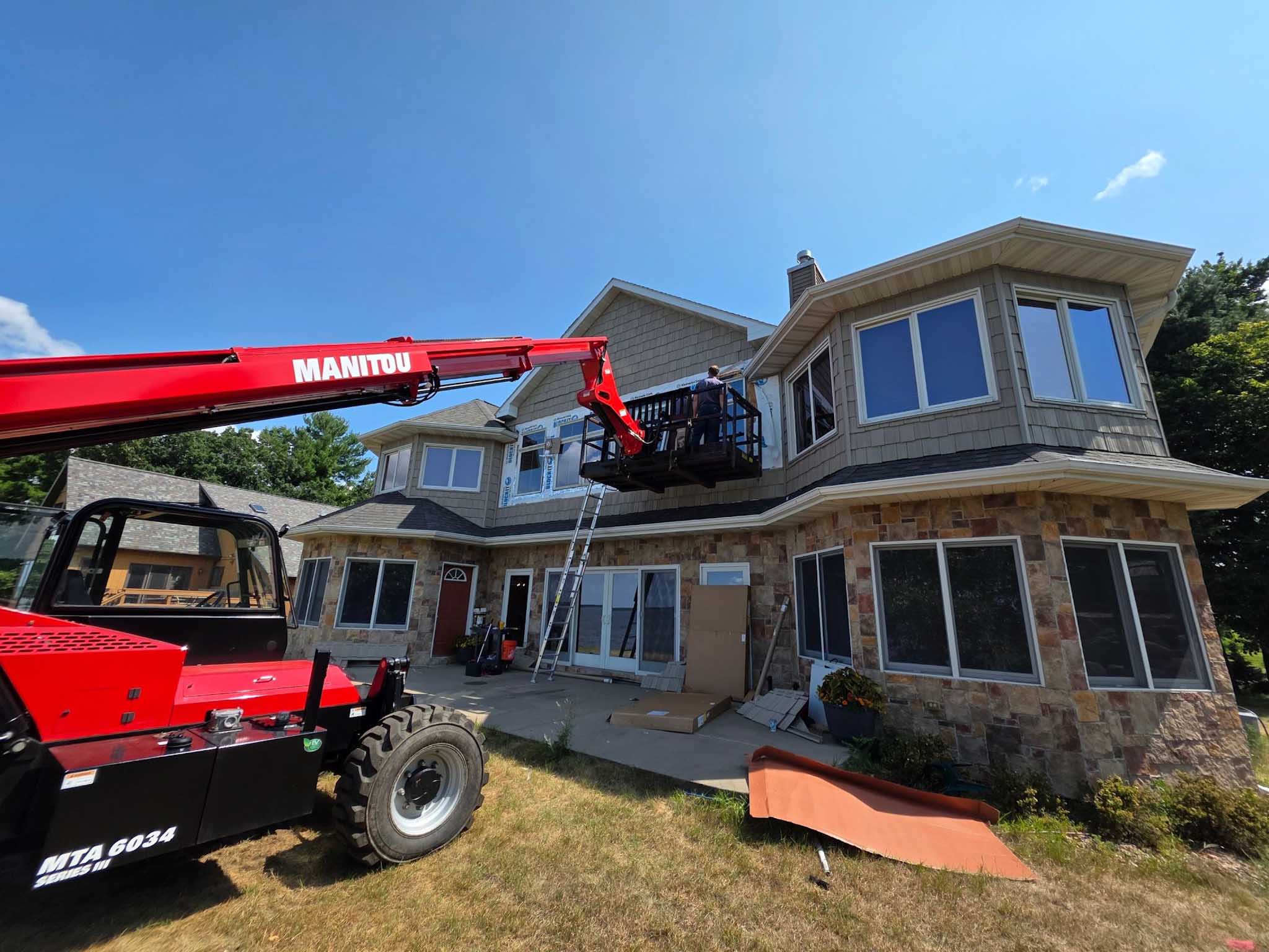 A red Manitou lift raises a balcony as replacement windows Wisconsin are installed on a sunny day.