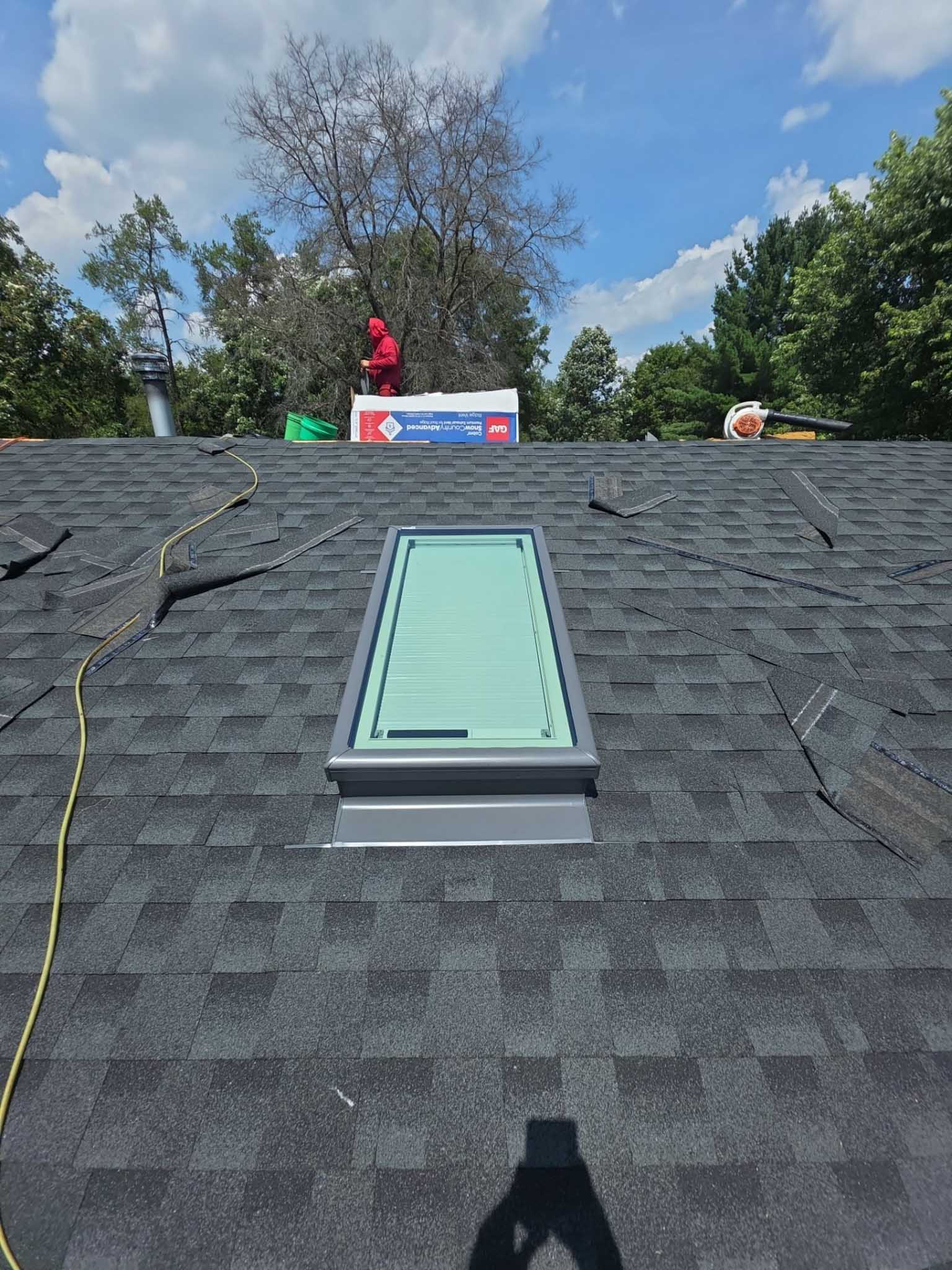 Gray shingled roof with skylight, tools, and a person in red near Replacement Windows Wisconsin.