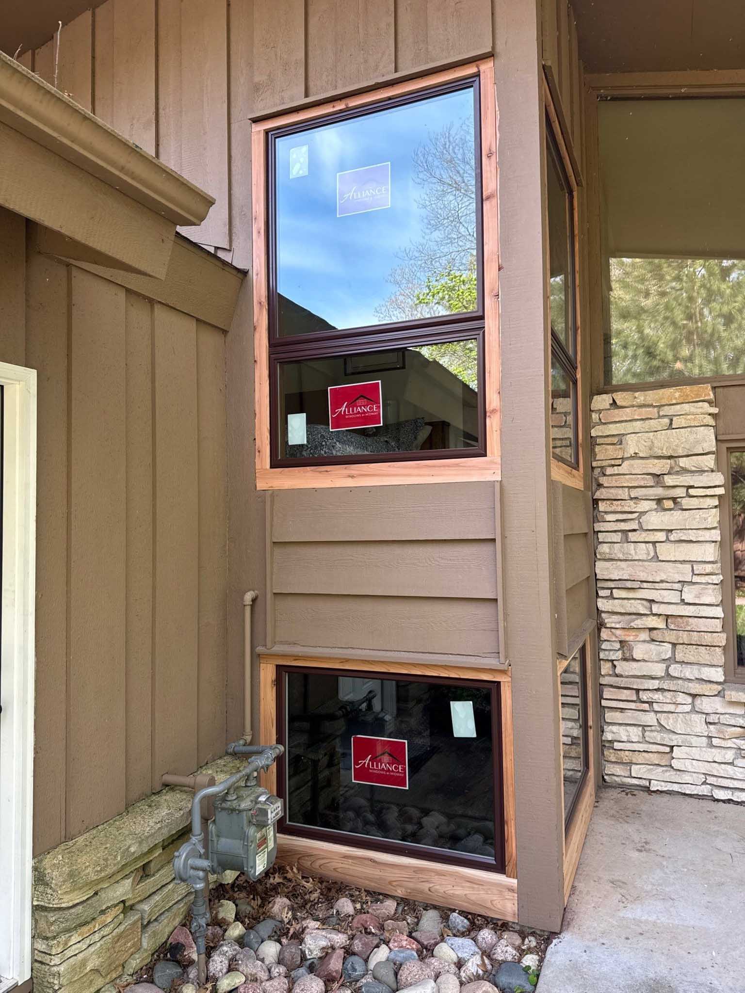 Three new Replacement Windows Wisconsin and Alliance stickers on a brown house with stone accents.