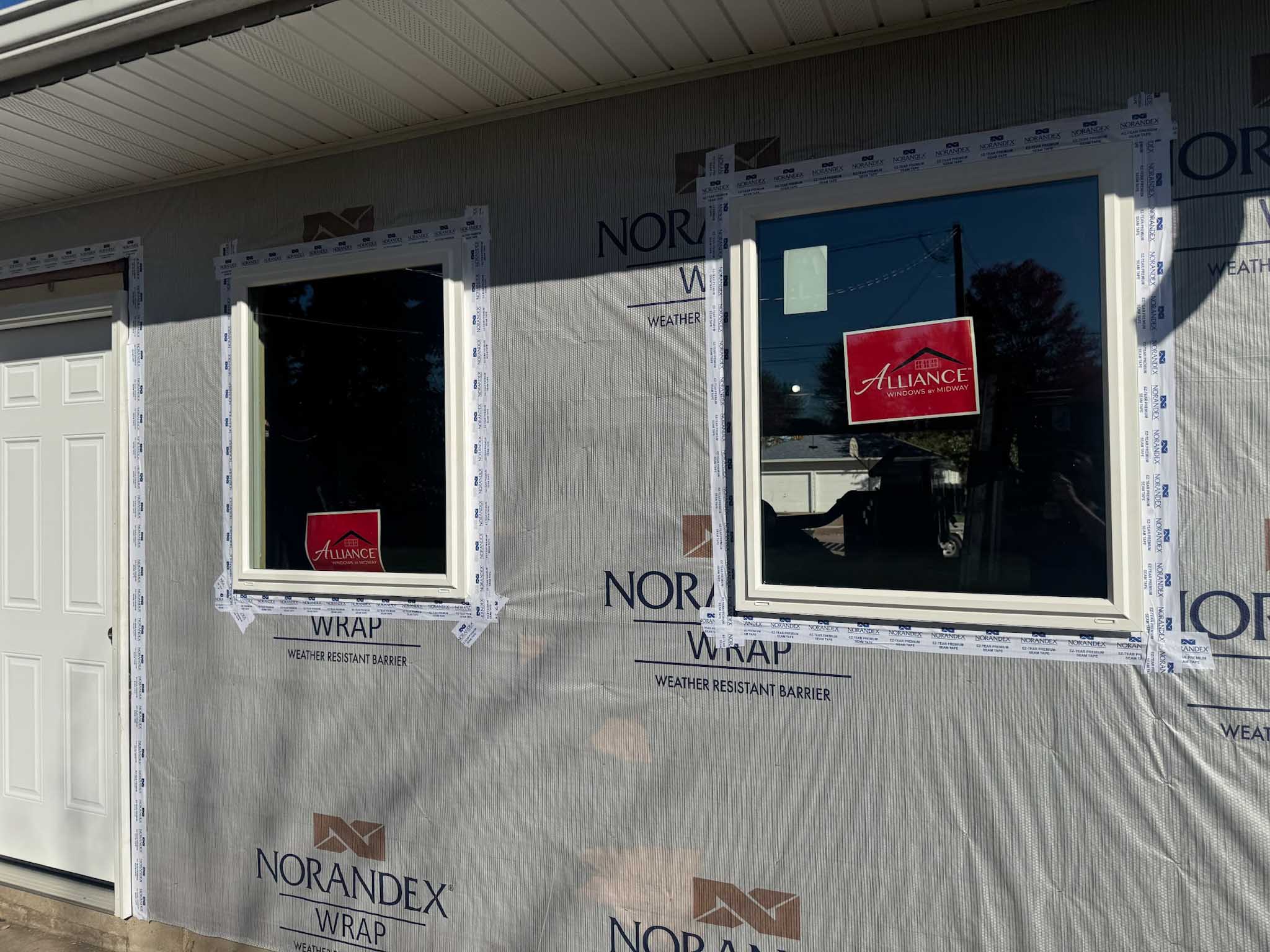 Two Replacement Windows Wisconsin installed in a Norandex-wrapped wall, sunlight casting shadows.