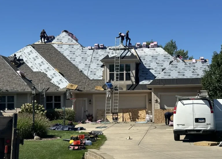 Workers reroofing a house, with tools and materials scattered on the driveway and roof.