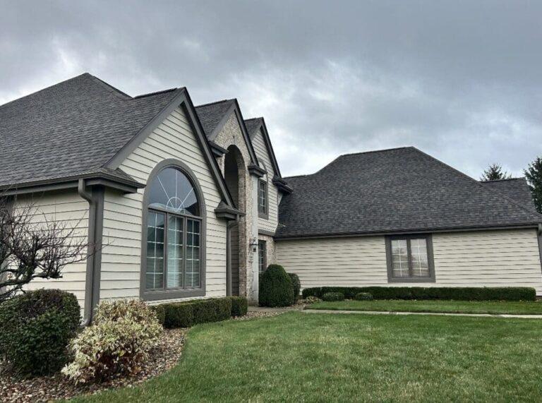 Two-story suburban house with gray siding, arched window, and a well-kept lawn under cloudy sky.